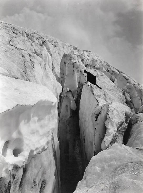 1912年，一名男子（图中右方的黑色人形）在雷尼尔峰东南侧直盯着分裂天堂冰河和考利兹冰河的冰隙。